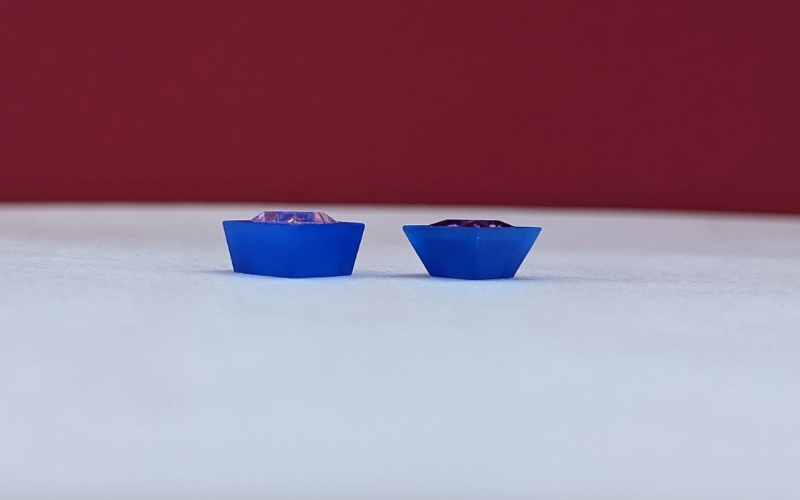 2 square settings, one has walls that are slightly tapered and the other one has extremely tapered walls. Both made from blue wax, stones inside are a pink and red cubic zirkonia