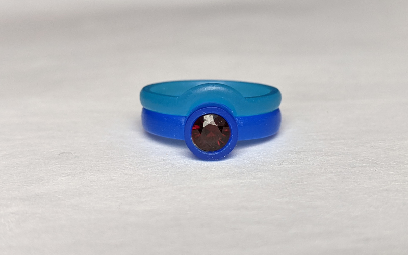 Blue wax ring with a round garnet in the middle and a turquoise wax ring that arches exactly around the setting