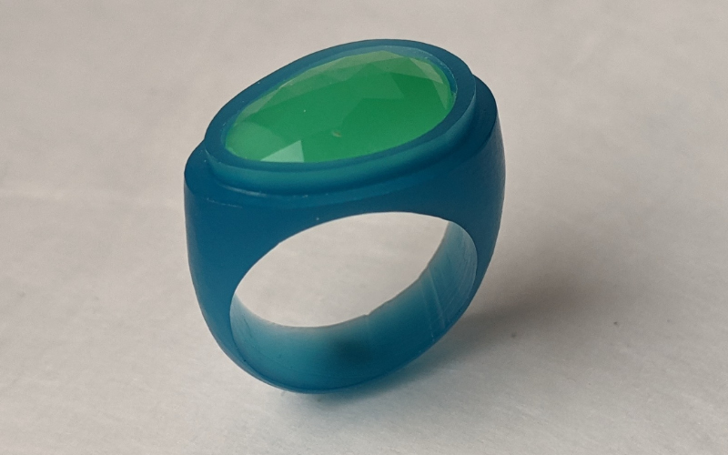 Chrysophrase ring in turquoise wax. The ring follows the shape of the stone and is smaller on the left side and wider on the right side