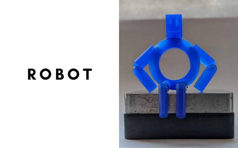 Robot: robot made from blue wax sitting on a steel block. His body is round and his limbs are bend at the elbows and knees