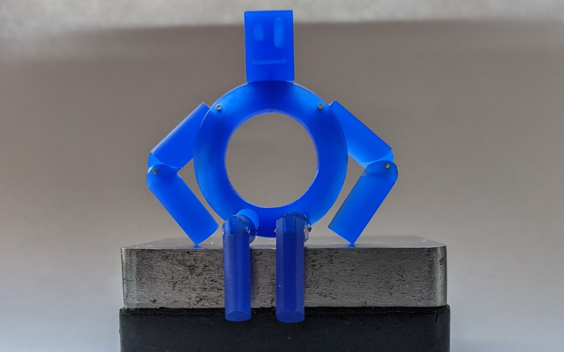 Robot from blue wax sitting on a steel block. Arms and legs are bend