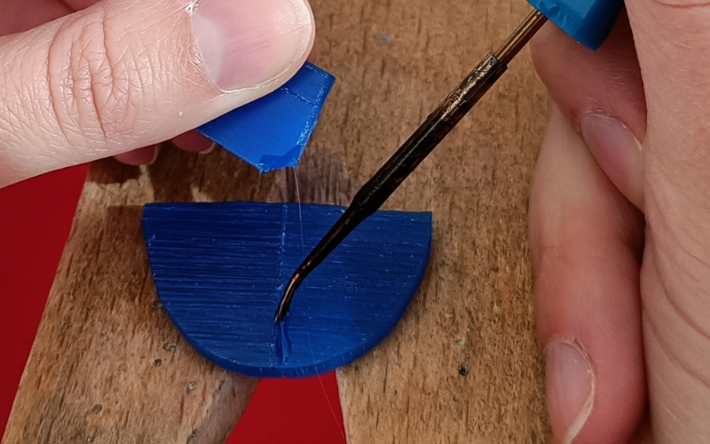 pieces of blue wax lying on bench peg. Hands holding a wax heating pen adding wax on the join