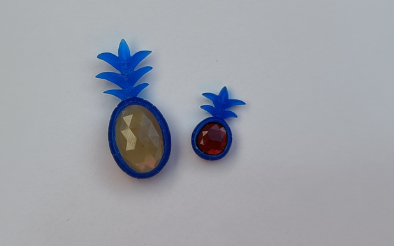2 wax pineapples, one with an oval yellow stone one with and oval red stone