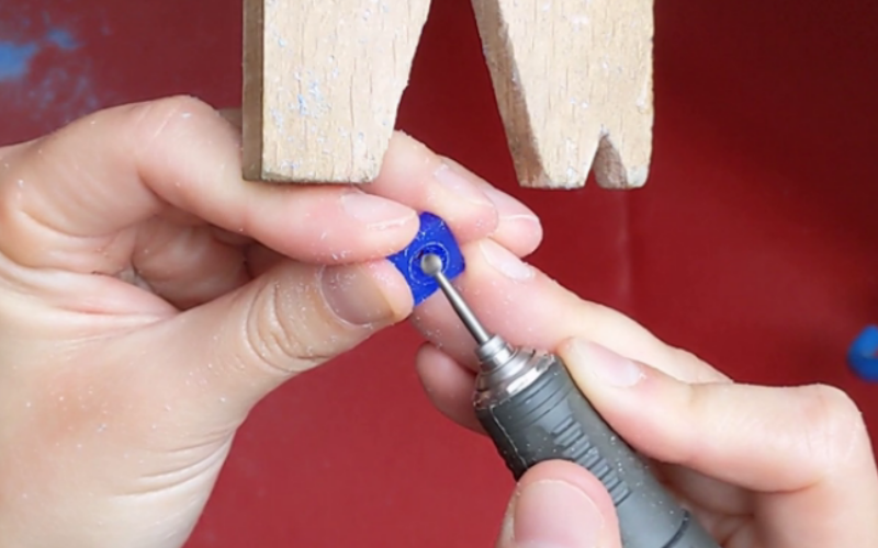 Left hand holding a piece of wax with a round cut out against a bench peg. Right hand holds a drill and is ball burring the inside shape.