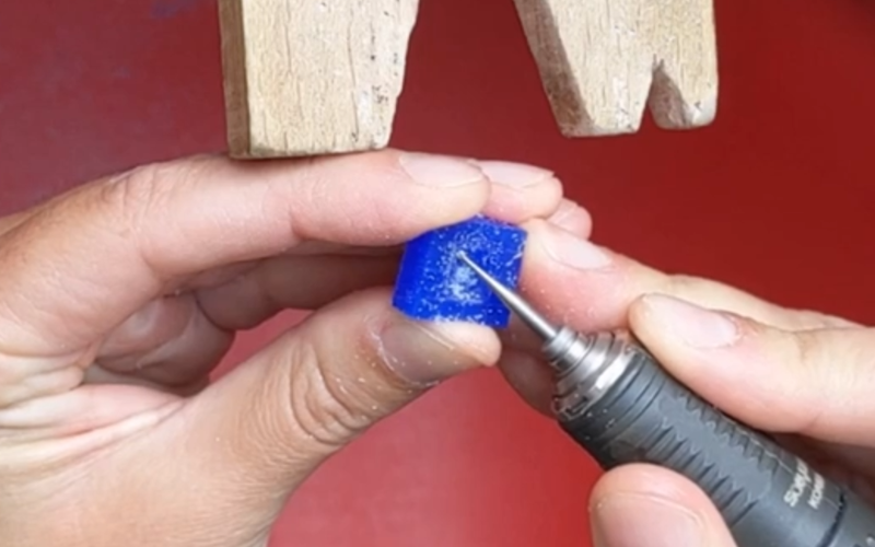 Close up of hands working at the bench. The left hand is holding a piece of blue wax and the right hand is ball burring the wax