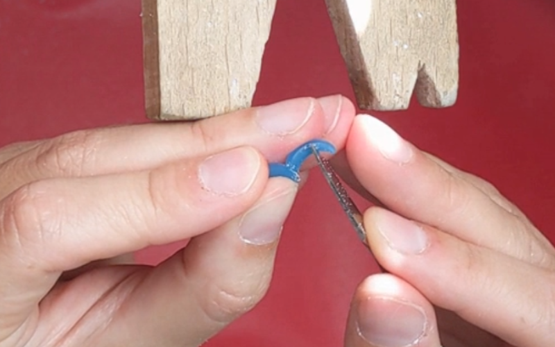 Close up of hands working at the bench.The left hand is holding a very small piece of turquoise wax between thumb and forefinger, resting part of it on the middlefinger. Right hand is using a carving tool to carve the part that is being supported on themiddle finger