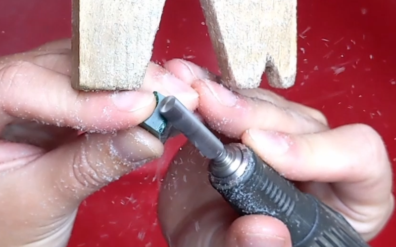 Close up of hands working at the bench. Both hands are touching each other and the peg.Left hand is holding a piece of green wax while the right hand is burring the wax