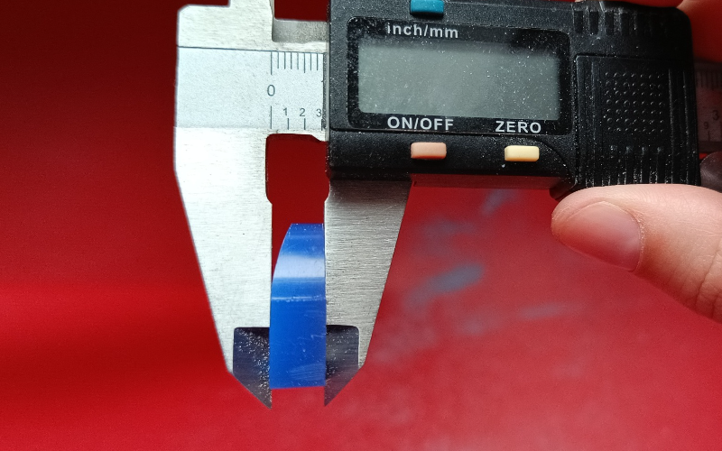 Close up of hands holding a piece of blue ring wax in calipers