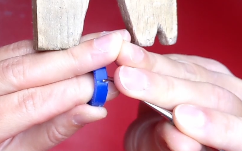 Close up of hands working at the bench. Both hands are touching each other. Left hand is holding a blue wax ring and left hand is using a carving tool on it