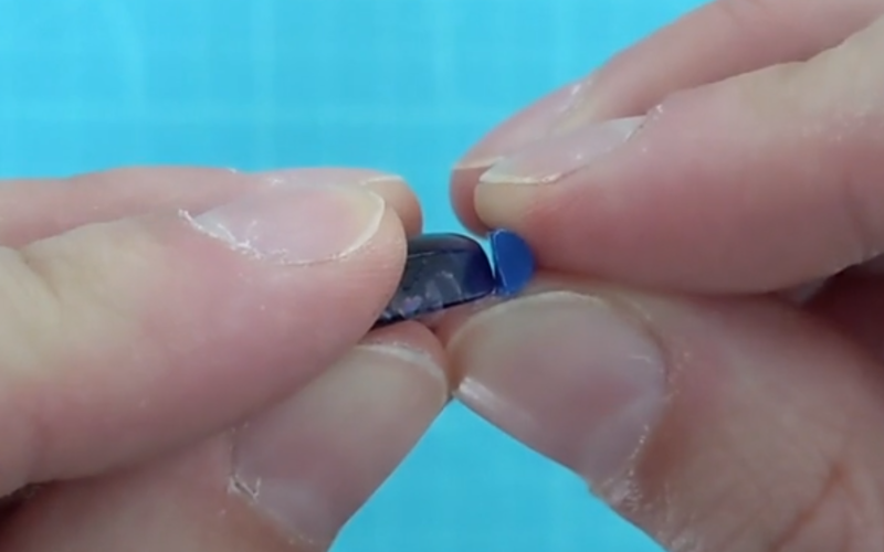 Close up of hands holding an amethyst stone showing the side profile with a piece of blue wax wire next to it to check how the height compares