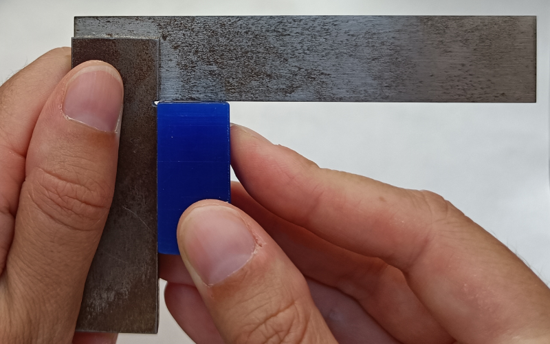 Close up of hands holding a set square and measuring a blue piece of wax in the corner. There is a gap visible on the top