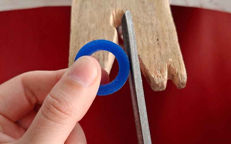 Close up of hands holding a blue wax ring, botgtom left corner is covered with a thumb. Other hand is holding a file on the right side of the ring