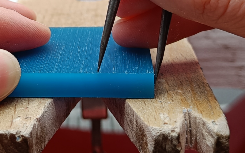 Hand holding a pair of dividers on the wax, the dividers are angled to the side. 