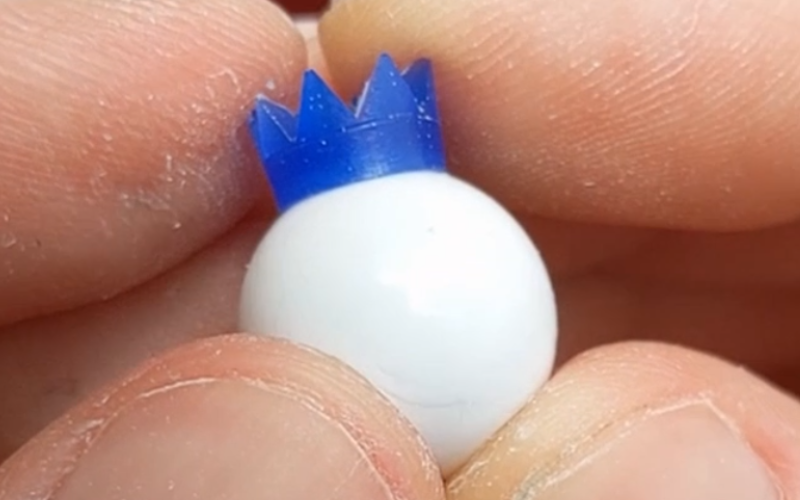  Close up of hands holding a bead with a small blue wax bead cap on top that's shaped like a crown