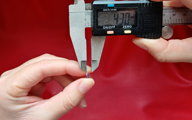 hands trying to measure the distance between girdle and culet of a gemstone with calipers