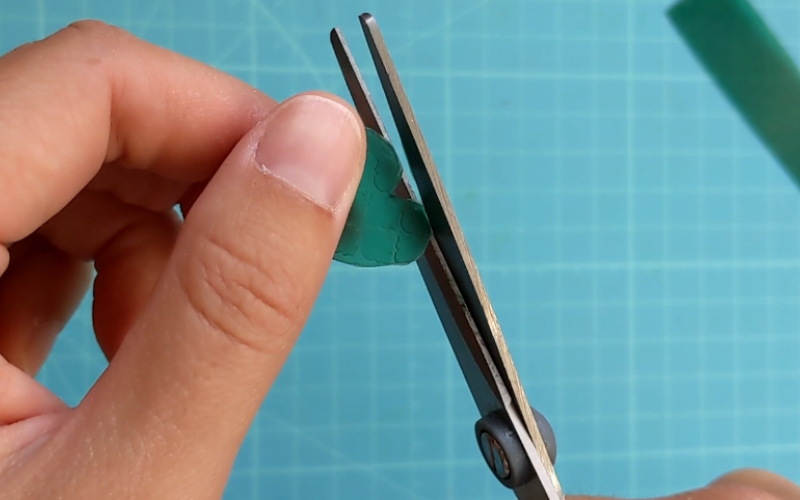 Close up of hands holding a piece of textured green sheet wax while cutting it into a heart shape with scissors