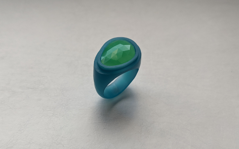 A diagonal ring from turquoise wax that's wider at one side than the other with a green stone