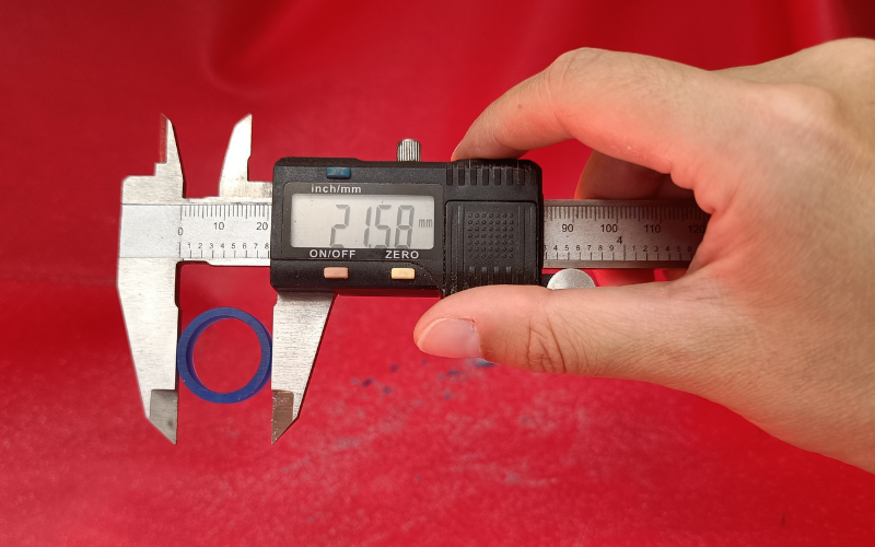 Hand holding calipers over a red bench skin, Calipers are measuring the outside of a ring, the display read 21.58mm