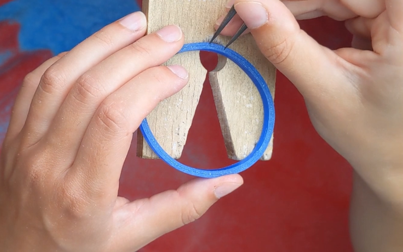 Close up of hands marking equal distances on the side of a blue wax bangle 
