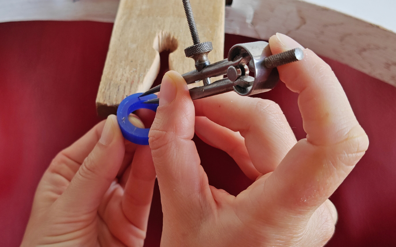 Close up of hands holding a piece of blue ring wax. Right hand is marking a line with dividers using the inside of the ring as a guide. Dividers are angled towrds the inisde of the ring and the point of the guiding leg of the divider is farther down in the ring