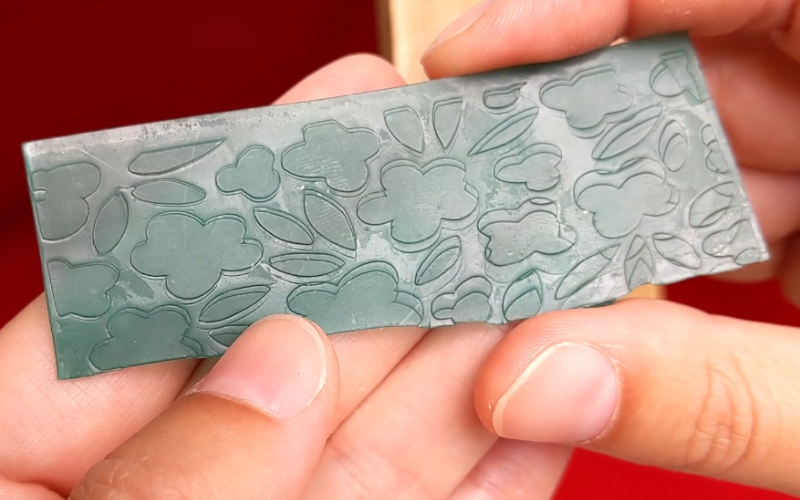 Close up of hands holding a piece of green textured sheet wax. The texture has double lines