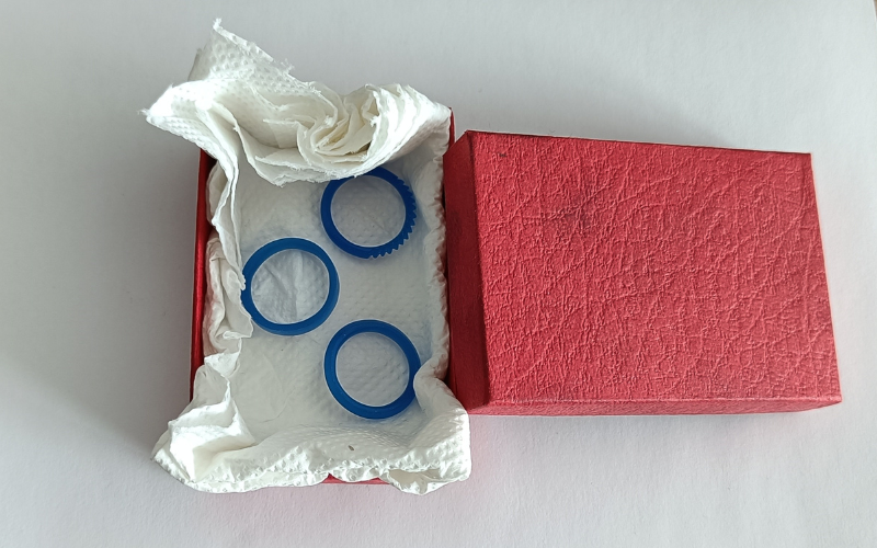 red cardboard box lined with kitchen roll paper and 3 blue wax rings lying on top