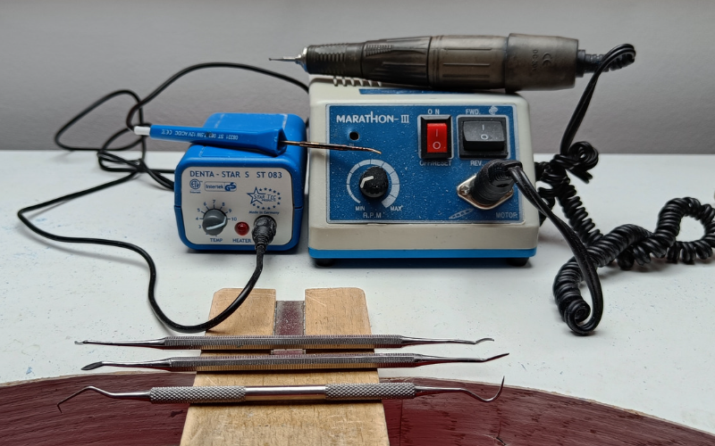 Bench with a micromotor, wax heating pen and 3 double sided carving tools on top 