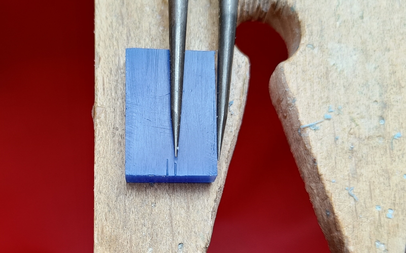 Close up of piece of blue wax with 2 small lines marked on it.