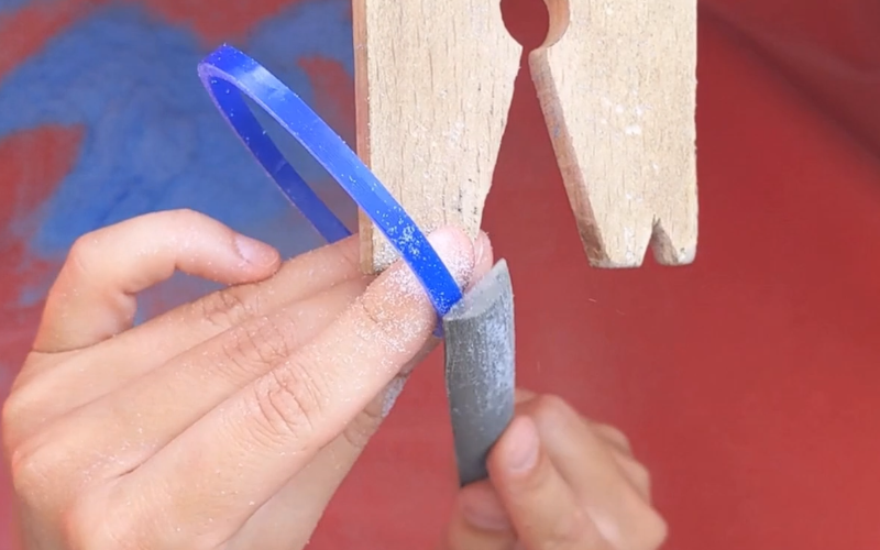 Close up of hands filing the outside of a blue wax bangle