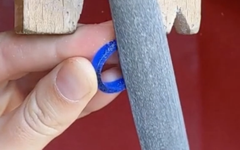 Hand holding a wax ring and other hand is filing the ring, you can see pen marks on the side of the ring that isn't being filed 