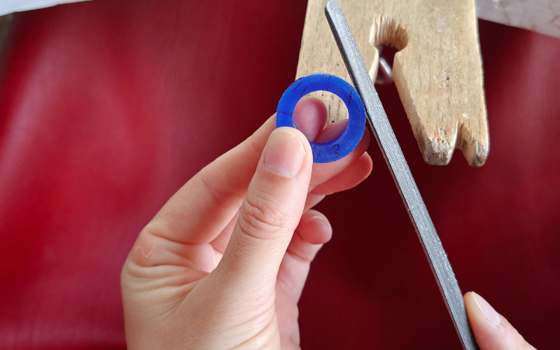 Close up of hands holding a piece of blue ring wax. Left hand is holding the ring in quarter 3, right hand is filing at quarter 1 which is in the best and easiest spot to work on