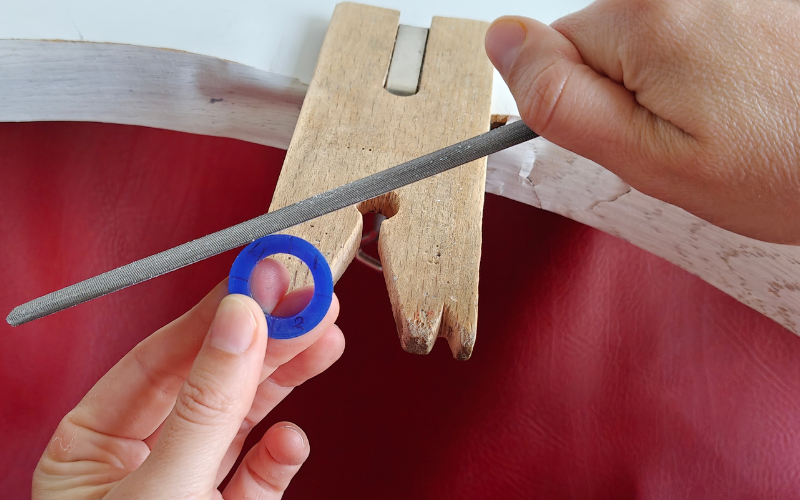 Close up of hands holding a piece of blue ring wax. Left hand is holding the ring in quarter 3, right hand is filing at quarter 4 which is in a more difficult to reach spot making filing uncomfortable