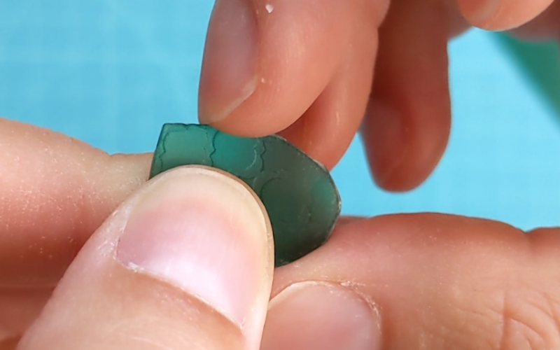 Close up of a piece of green sheet wax, fingernail is scraping around the edge to smoothen it