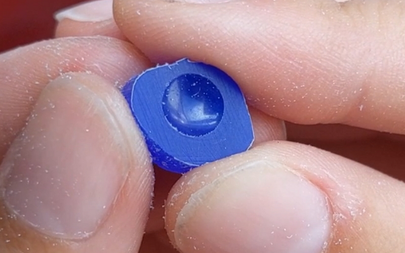  Close up of hands holding a small piece of blue wax with a perfect round imprint in the wax