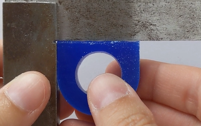 Close up of hands holding a blue wax ring against a set square. There are some gaps visible between the ring and the arm of the set square so the top of the ring is not flat yet