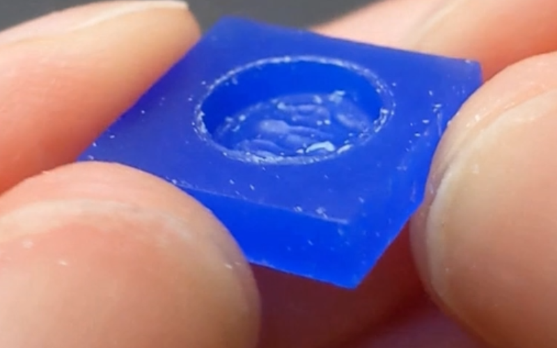 Close up of hands holding a piece of blue wax with a round opening carved away. the walls on the inside of the opening flat and there's a definite distinction between it and the bottom