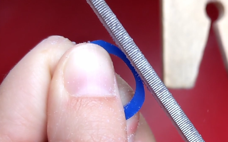 Close up of hands holding a blue wax ring. A file is pushing down on the ring to demonstrate how it flexes without support.