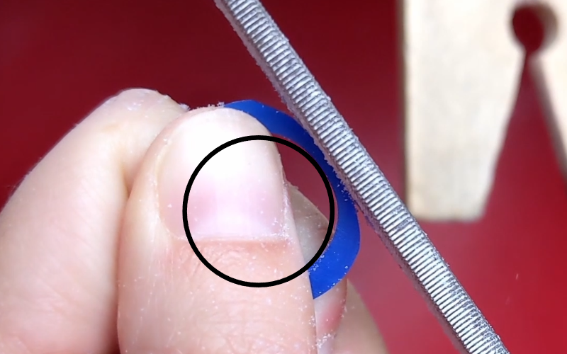 Close up of hands holding a blue wax ring. A file is pushing down on the ring to demonstrate how it flexes without support. A black circle is drawn on the inside of the ring to show that the inside of teh ring is no longer round. 
