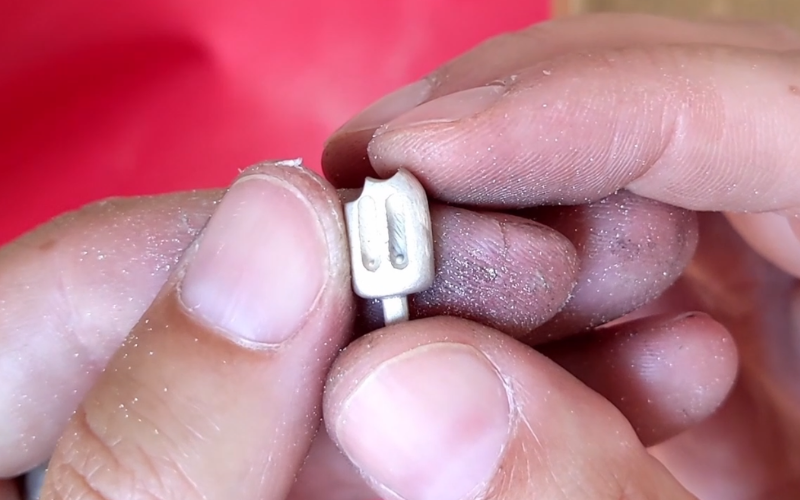 close up of hands holding a silver ice cream shape. In one of the hollow lines you can see a granule