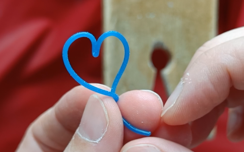 Close up of hands holding a piece of blue wax wire formed into a heart