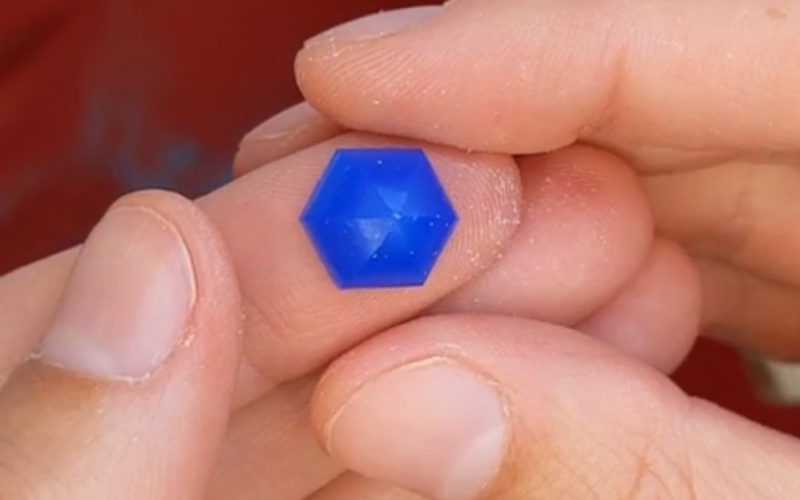 Close up of hands holding a piece of blue wax that's carved in a hexagonal shape