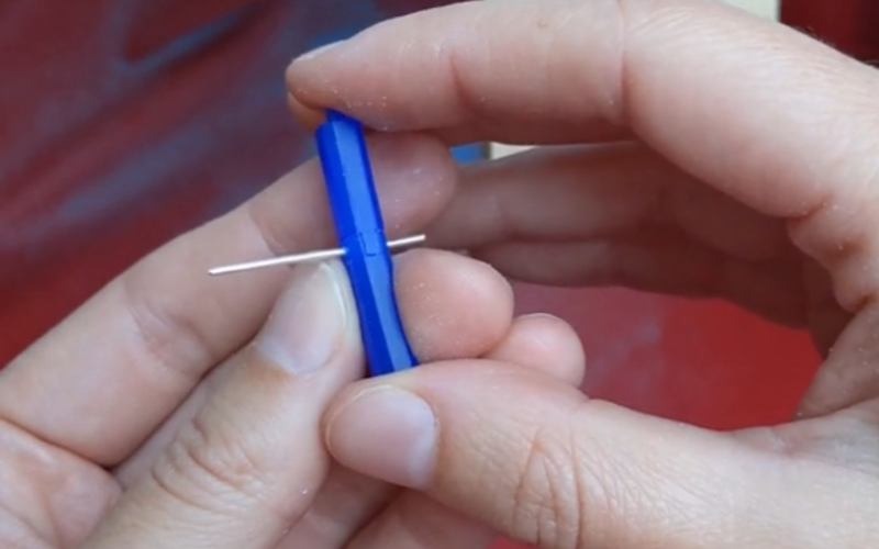 close up of hands holding a piece of blue wax. There's a piece of silver wire going through the centre where 2 separate pieces are attaced together
