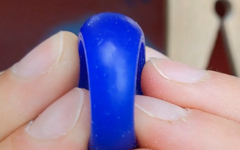 Close up of hands holding a blue wax ring, you can only see the part right in front, the rest of the ring is hidden from view by th efront section