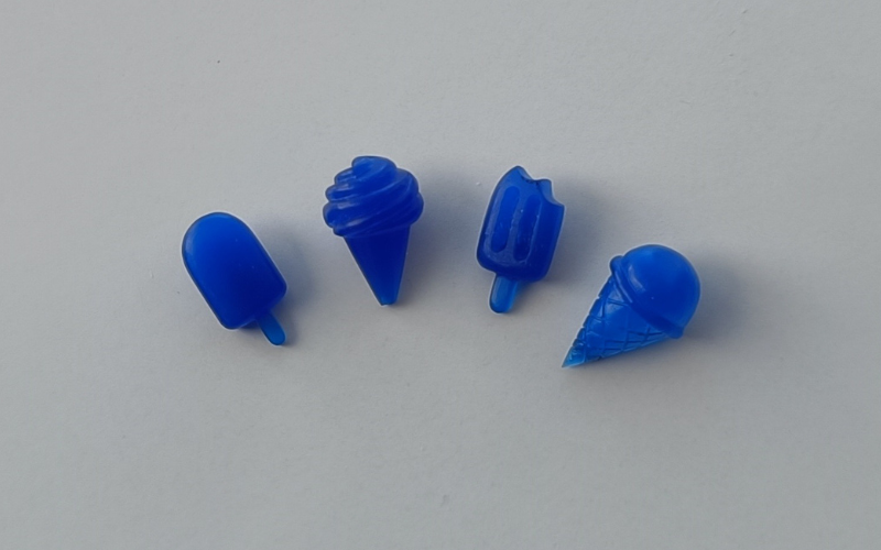 4 ice cream charms made from blue wax. From left to right an ice lolly, a soft serve, an ice lolly with a bite taken out and a single scoop ice cream