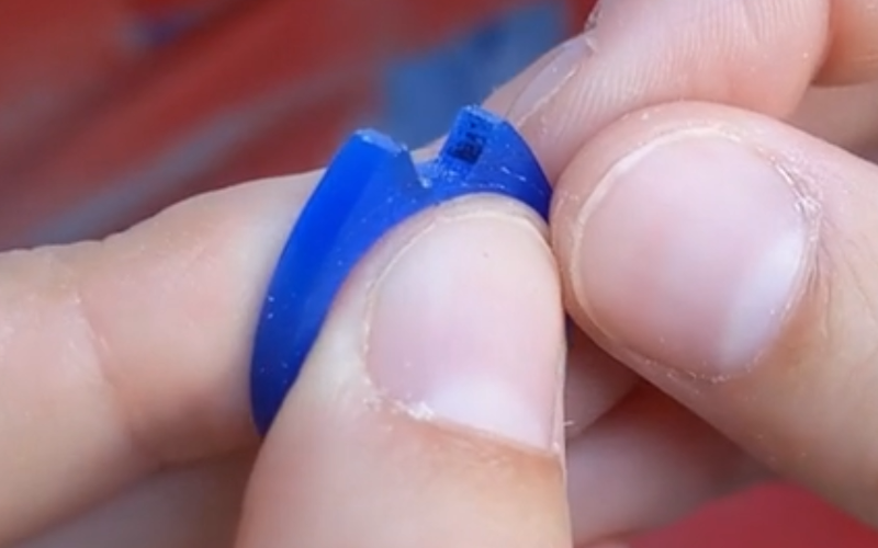 Close up of a piece of blue ring wax parts of the ring have black ink on them. 