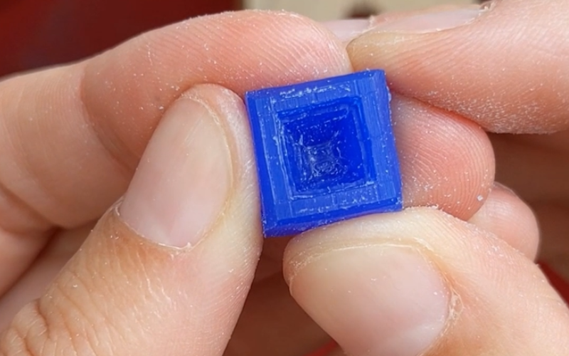 Close up of hands holding a piece of blue wax with a square opening removed. Walls are cleaner, more wax removed