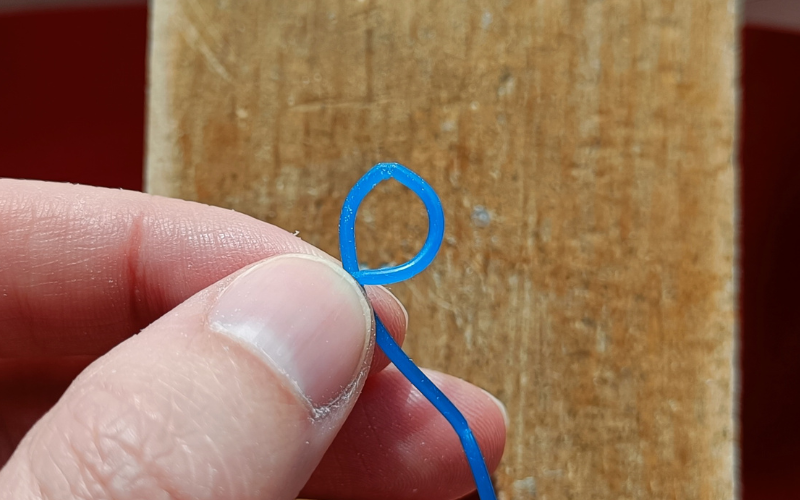Close up of hands holding a piece of blue wax wire that's formed into a circle, top of the circle is kinked and flat
