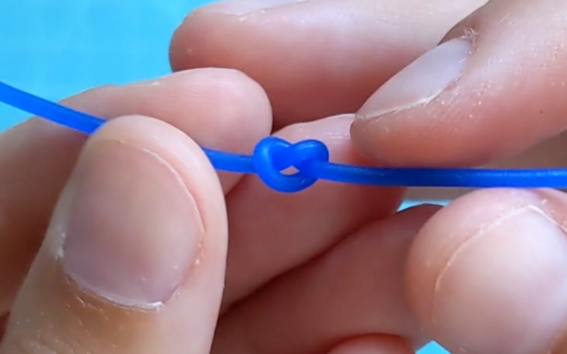 Close up of hands holding a piece of blue wax wire with a tight knot in the middle