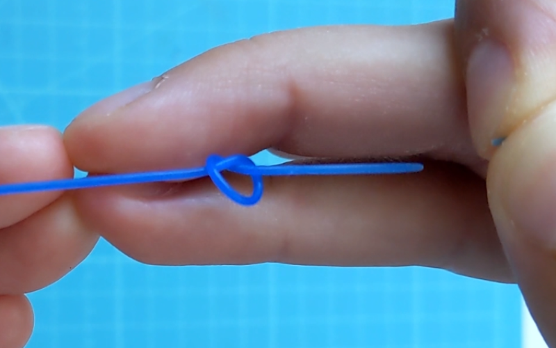Close up of hands holding a piece of blue wax wire with a very loose knot in the middle, wire is broken from pulling too much