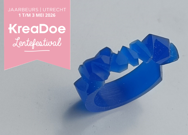 Fingers holding a blue wax ring with cut out rock like pattern on top. In the top left corner is the kreadoe banner announcing the dates 1-3 of May 2026